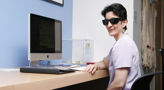 woman seated at her computer work station, wearing sunglasses